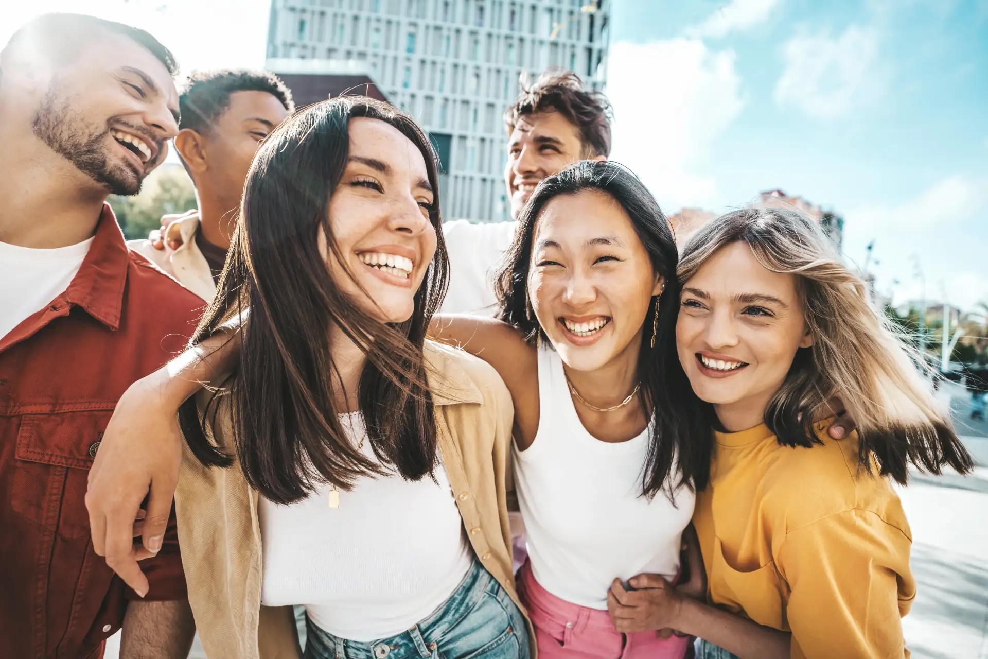 A diverse group of friends laugh and walk while hugging and draping their arms over one another.